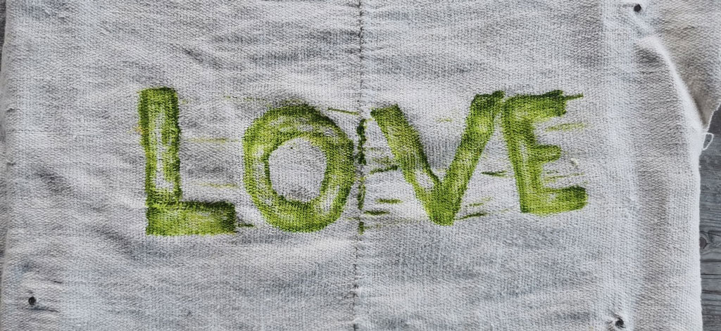 Grüne Buchstaben auf grauem Stoff zeigen das Wort "LOVE".
